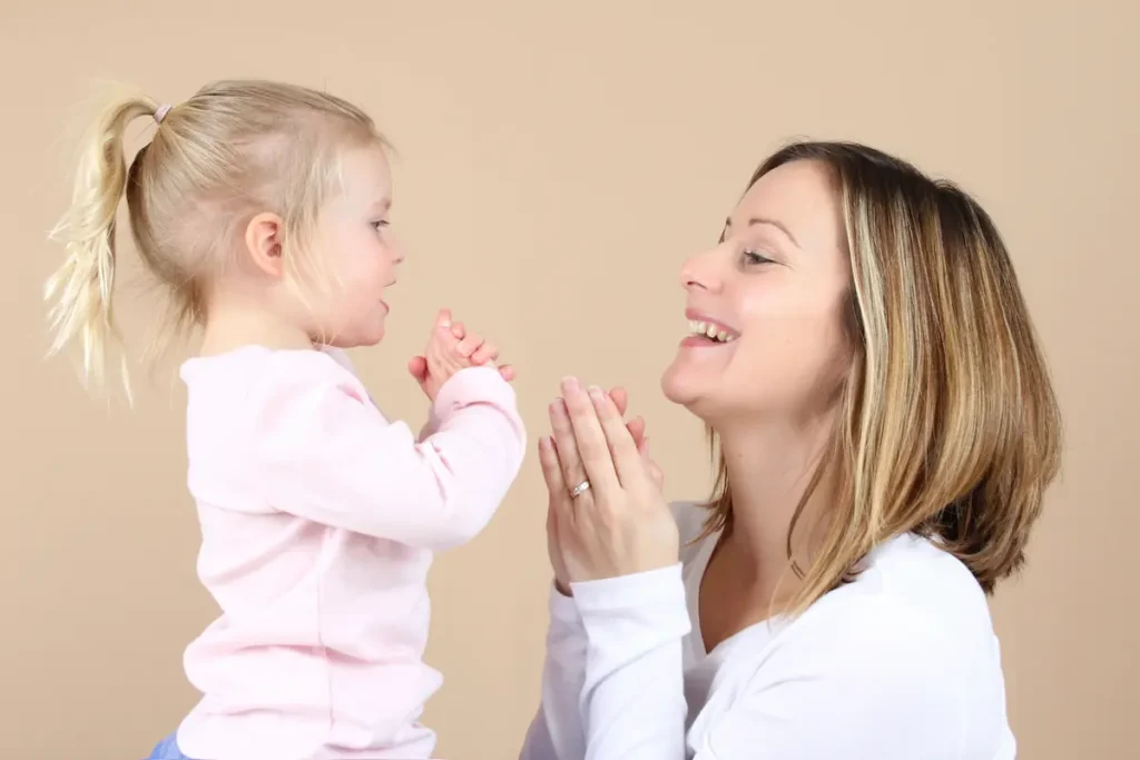 Kvinna som pratar med sin lilla dotter. De klappar händerna och ler mot varandra.